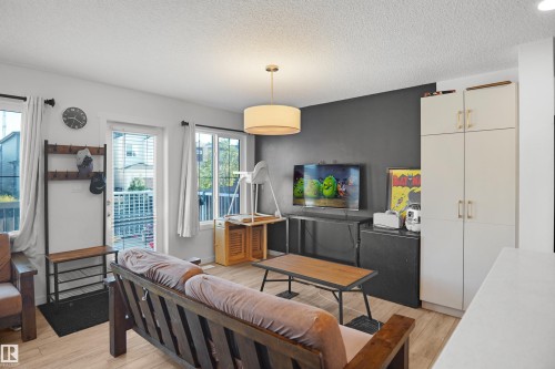 Open-concept living area featuring wood-finish flooring, a contemporary pendant light fixture, and a dark accent wall - #42 19904 31 Av Nw, Edmonton, AB - Indoor Photo Showing Living Room