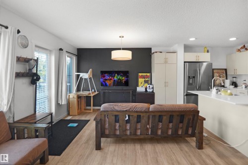 Open-concept living space featuring wood-finish flooring, a contemporary ceiling light fixture, and a kitchen area with light cabinetry and stainless steel appliances - #42 19904 31 Av Nw, Edmonton, AB - Indoor