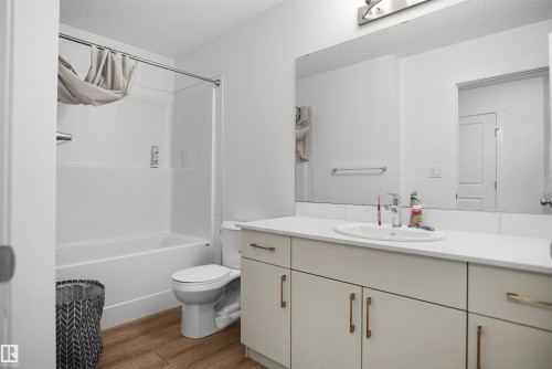 Bathroom featuring a tub/shower combination, light wood-finish flooring, a toilet, a vanity with an integrated sink, and a large wall-mounted mirror - #42 19904 31 Av Nw, Edmonton, AB - Indoor Photo Showing Bathroom