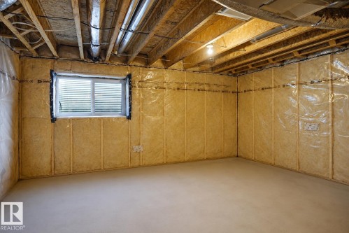 Unfinished lower level featuring an egress window, exposed wood ceiling joists, insulation, and concrete flooring - #42 19904 31 Av Nw, Edmonton, AB - Indoor Photo Showing Basement