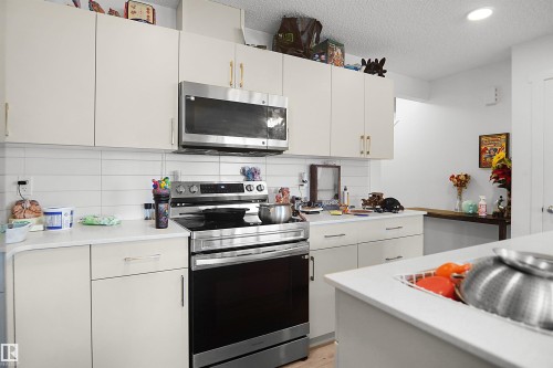 Kitchen featuring stainless steel appliances, white subway tile backsplash, light-toned cabinetry, and solid surface countertops - #42 19904 31 Av Nw, Edmonton, AB - Indoor Photo Showing Kitchen