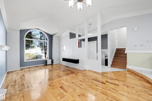 Spacious living area featuring polished wood-finish flooring, a grand arched window, vaulted ceilings, a contemporary chandelier, and a built-in floating shelf - 4639 10 Avenue Nw, Edmonton, AB - Indoor Photo Showing Other Room With Fireplace