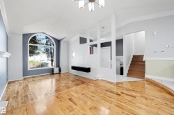 Spacious living area featuring polished wood-finish flooring, a grand arched window, vaulted ceilings, a contemporary chandelier, and a built-in floating shelf - 
