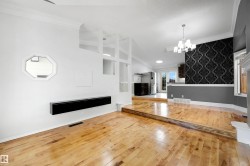 Open-concept living space featuring wood-finish flooring, a contemporary floating media console, a decorative octagon window, an accent wall with patterned wallpaper, and a multi-tiered ceiling design - 