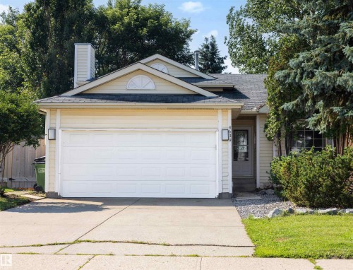 Cream-colored siding exterior featuring a white garage door, a front entry door with a storm door, and decorative half-round window trim on the front gable - 4639 10 Avenue Nw, Edmonton, AB - Outdoor