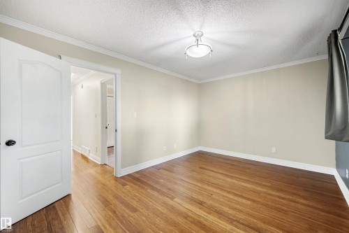 Spacious room featuring rich wood-finish flooring, crisp white baseboards and crown molding, a white ceiling light fixture, and a solid white interior door with a black handle - 4639 10 Avenue Nw, Edmonton, AB - Indoor Photo Showing Other Room