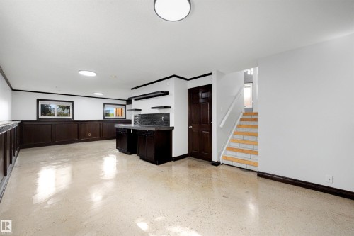 Spacious room with light-colored flooring, dark wood paneling, and an integrated wet bar featuring dark cabinetry and a dark countertop - 4639 10 Avenue Nw, Edmonton, AB - Indoor Photo Showing Other Room