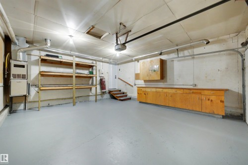 Spacious garage featuring a light gray floor, built-in wooden shelving, integrated cabinetry, a wooden countertop workstation, and an overhead garage door mechanism - 4639 10 Avenue Nw, Edmonton, AB - Indoor Photo Showing Garage