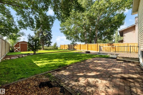 Expansive backyard featuring a brick paver patio, a raised wood deck with railings, a privacy fence, mature trees, and a storage shed - 4639 10 Avenue Nw, Edmonton, AB - Outdoor With Backyard