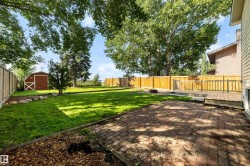 Expansive backyard featuring a brick paver patio, a raised wood deck with railings, a privacy fence, mature trees, and a storage shed - 