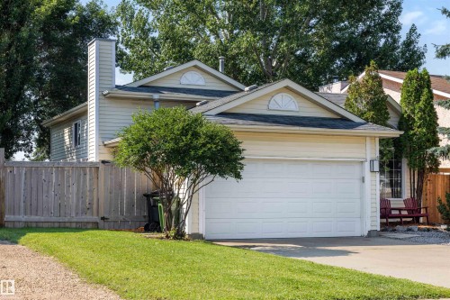 Light-toned siding exterior featuring a prominent front-facing garage, a decorative gable vent, a tall chimney, a private wooden fence, and a concrete driveway - 4639 10 Avenue Nw, Edmonton, AB - Outdoor