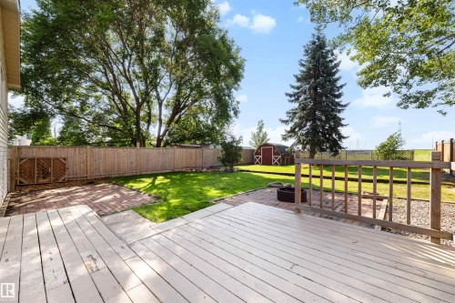 Expansive backyard featuring a wood deck, brick patio, mature trees, manicured lawn, and privacy fencing - 4639 10 Avenue Nw, Edmonton, AB - Outdoor With Deck Patio Veranda With Backyard