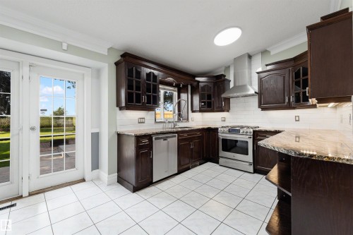 Kitchen featuring dark wood cabinetry, granite countertops, and stainless steel appliances - 4639 10 Avenue Nw, Edmonton, AB - Indoor Photo Showing Kitchen With Double Sink
