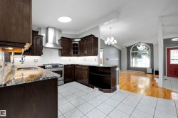 Kitchen featuring rich wood cabinetry, patterned stone countertops, a stainless steel range with a ventilation hood, and white tile flooring - 