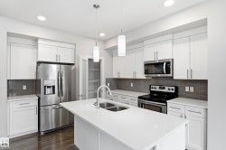 Kitchen featuring a large central island with a double basin sink and a high-arc faucet, stainless steel appliances, white cabinetry with silver hardware, grey subway tile backsplash, and recessed lighting - 