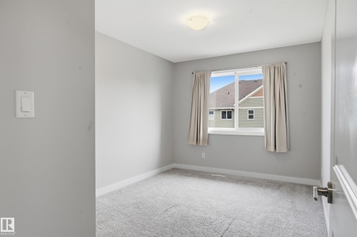 Carpeted room featuring a large window, neutral wall paint, white trim, and a ceiling-mounted light fixture - 1860 Keene Crescent Sw, Edmonton, AB - Indoor Photo Showing Other Room