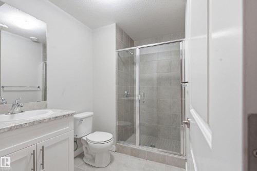Bathroom featuring a glass-enclosed shower with tile surround, white vanity with stone-finish countertop, undermount sink, and modern brushed nickel fixtures - 1860 Keene Crescent Sw, Edmonton, AB - Indoor Photo Showing Bathroom