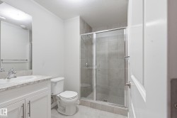 Bathroom featuring a glass-enclosed shower with tile surround, white vanity with stone-finish countertop, undermount sink, and modern brushed nickel fixtures - 