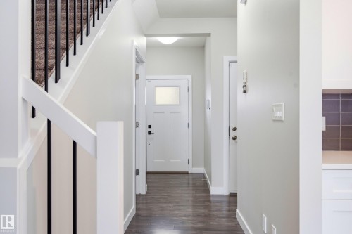 Entryway featuring wood-finish flooring, white trim, and a white staircase with black iron spindles and carpeted treads - 1860 Keene Crescent Sw, Edmonton, AB - Indoor Photo Showing Other Room