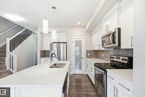 Bright kitchen featuring a substantial island with dual sinks, white cabinetry, stainless steel appliances, and wood-finish flooring - 1860 Keene Crescent Sw, Edmonton, AB - Indoor Photo Showing Kitchen With Double Sink With Upgraded Kitchen