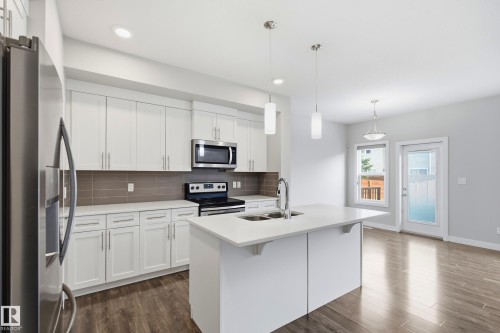 Modern kitchen featuring white cabinetry, stainless steel appliances, a white island with an undermount sink, and wood-finish flooring - 1860 Keene Crescent Sw, Edmonton, AB - Indoor Photo Showing Kitchen With Double Sink With Upgraded Kitchen