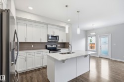 Modern kitchen featuring white cabinetry, stainless steel appliances, a white island with an undermount sink, and wood-finish flooring - 