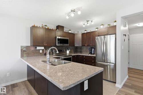 Kitchen featuring dark wood cabinetry, stainless steel appliances, a double basin sink, and wood-finish flooring - 3606 Whitelaw Bay Nw, Edmonton, AB - Indoor Photo Showing Kitchen With Double Sink With Upgraded Kitchen