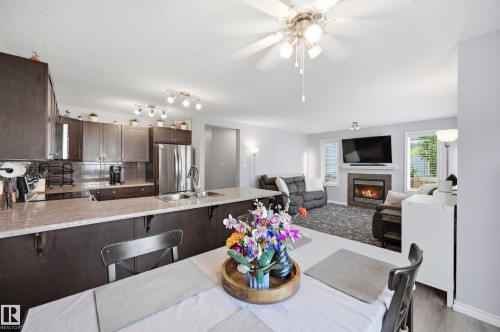 Open-concept living space featuring a kitchen with dark cabinetry, light-toned countertops, and stainless steel appliances - 3606 Whitelaw Bay Nw, Edmonton, AB - Indoor Photo Showing Dining Room With Fireplace