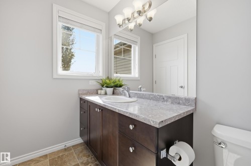 Bathroom featuring a wood-finish vanity with an integrated white sink, a light-toned countertop, and an overhead vanity light fixture - 3606 Whitelaw Bay Nw, Edmonton, AB - Indoor Photo Showing Bathroom