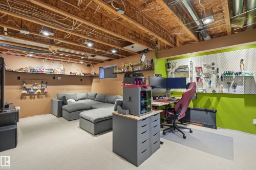 Finished basement space featuring exposed wood joist ceiling, recessed lighting, carpet flooring, a built-in wall shelf, and a designated workspace with pegboard storage - 3606 Whitelaw Bay Nw, Edmonton, AB - Indoor Photo Showing Basement