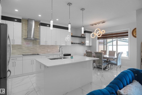 Contemporary kitchen featuring white high-gloss cabinetry, a central island with an undermount sink, and a stainless steel range hood - 4003 39 Street, Beaumont, AB - Indoor Photo Showing Kitchen With Upgraded Kitchen