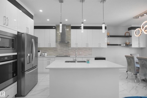Modern kitchen featuring a large center island, integrated stainless steel appliances, white cabinetry with contemporary hardware, a tiled backsplash, and recessed and pendant lighting - 4003 39 Street, Beaumont, AB - Indoor Photo Showing Kitchen With Upgraded Kitchen