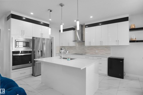 Modern kitchen featuring a large central island, stainless steel appliances, white flat-panel cabinetry, quartz countertops, and mosaic tile backsplash - 4003 39 Street, Beaumont, AB - Indoor Photo Showing Kitchen With Upgraded Kitchen