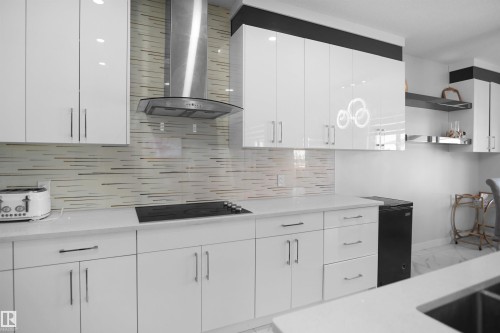 Modern kitchen featuring white high-gloss cabinetry with bar pulls, a stainless steel range hood, an integrated cooktop, a linear tile backsplash, and light-toned countertops - 4003 39 Street, Beaumont, AB - Indoor Photo Showing Kitchen With Upgraded Kitchen