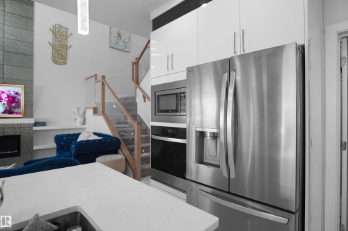 Modern kitchen featuring glossy white cabinetry, stainless steel French-door refrigerator with ice and water dispenser, built-in microwave, and integrated oven - 4003 39 Street, Beaumont, AB - Indoor Photo Showing Kitchen