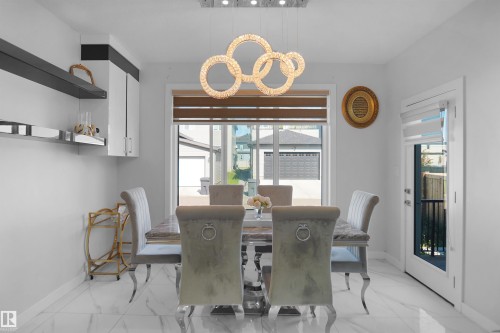 Bright dining area featuring a modern chandelier, white cabinetry with dark shelving, and large windows with blinds - 4003 39 Street, Beaumont, AB - Indoor Photo Showing Dining Room
