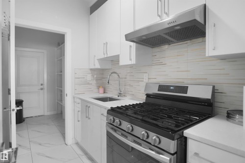 Modern kitchen featuring white cabinetry with silver hardware, a stainless steel gas range with a matching range hood, and a geometric-patterned backsplash - 4003 39 Street, Beaumont, AB - Indoor Photo Showing Kitchen With Upgraded Kitchen