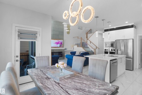 Open-concept living space with a polished tile floor, a contemporary kitchen island with a built-in sink, stainless steel appliances, a modern fireplace, and a glass-paneled staircase - 4003 39 Street, Beaumont, AB - Indoor