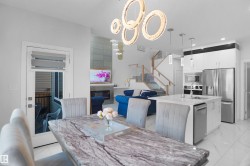 Open-concept living space with a polished tile floor, a contemporary kitchen island with a built-in sink, stainless steel appliances, a modern fireplace, and a glass-paneled staircase - 