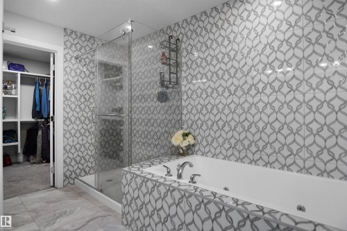Contemporary bathroom featuring a jetted soaking tub, glass-enclosed shower, patterned wall tile, and large format floor tile - 4003 39 Street, Beaumont, AB - Indoor Photo Showing Bathroom
