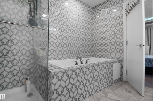 Bathroom featuring a built-in tub with chrome fixtures, glass shower enclosure, patterned wall tile, and stone-finish floor tile - 4003 39 Street, Beaumont, AB - Indoor Photo Showing Bathroom