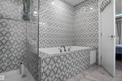 Bathroom featuring a built-in tub with chrome fixtures, glass shower enclosure, patterned wall tile, and stone-finish floor tile - 