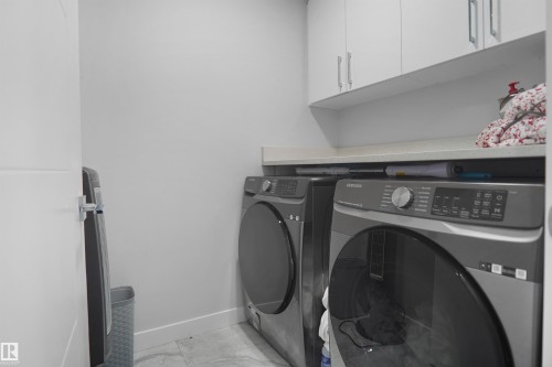 Laundry area featuring white cabinetry with silver hardware, an integrated countertop, and tiled flooring - 4003 39 Street, Beaumont, AB - Indoor Photo Showing Laundry Room