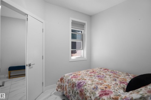 Bright room featuring a single window with a roller blind, a solid white door with chrome hardware, and white-hued walls - 4003 39 Street, Beaumont, AB - Indoor Photo Showing Bedroom