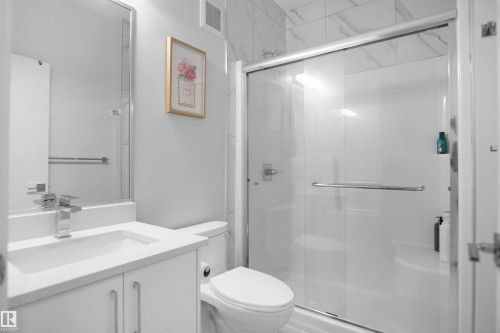 Bathroom featuring a contemporary vanity with a white countertop and undermount sink, a chrome faucet, a mirrored wall, and a glass-enclosed shower with white paneling and a tiled upper wall - 4003 39 Street, Beaumont, AB - Indoor Photo Showing Bathroom