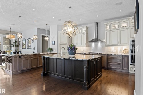 Kitchen with light stone countertops, pendant lighting, wall chimney range hood, dark wood finished floors, and a textured ceiling - 2796 Wheaton Drive Nw, Edmonton, AB - Indoor Photo Showing Kitchen With Upgraded Kitchen