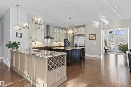 Kitchen featuring a chandelier, light stone countertops, glass insert cabinets, decorative light fixtures, and wall chimney range hood - 2796 Wheaton Drive Nw, Edmonton, AB - Indoor Photo Showing Kitchen With Upgraded Kitchen