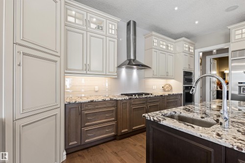 Kitchen featuring tasteful backsplash, wall chimney range hood, dark brown cabinets, light stone countertops, and a textured ceiling - 2796 Wheaton Drive Nw, Edmonton, AB - Indoor Photo Showing Kitchen With Upgraded Kitchen