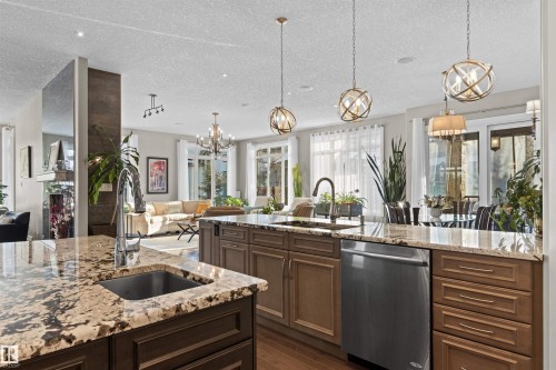 Kitchen featuring a chandelier, decorative light fixtures, dishwasher, light stone countertops, and open floor plan - 2796 Wheaton Drive Nw, Edmonton, AB - Indoor Photo Showing Kitchen With Upgraded Kitchen