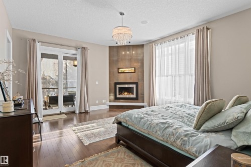 Bedroom featuring dark wood-style floors, a tile fireplace, access to exterior, a chandelier, and a textured ceiling - 2796 Wheaton Drive Nw, Edmonton, AB - Indoor With Fireplace